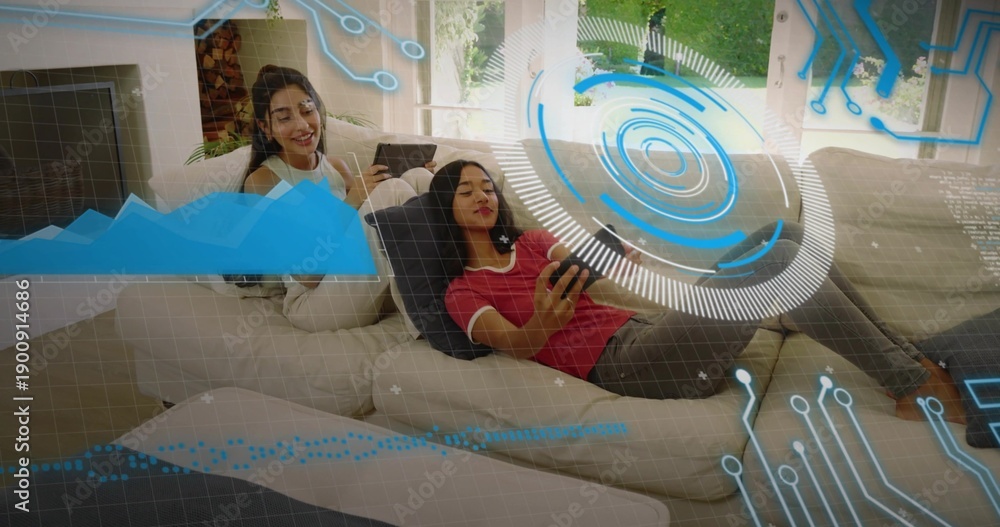 Fototapeta premium Lounging two women in red shirt and white top, scrolling smartphone and tablet on sectional, HUD