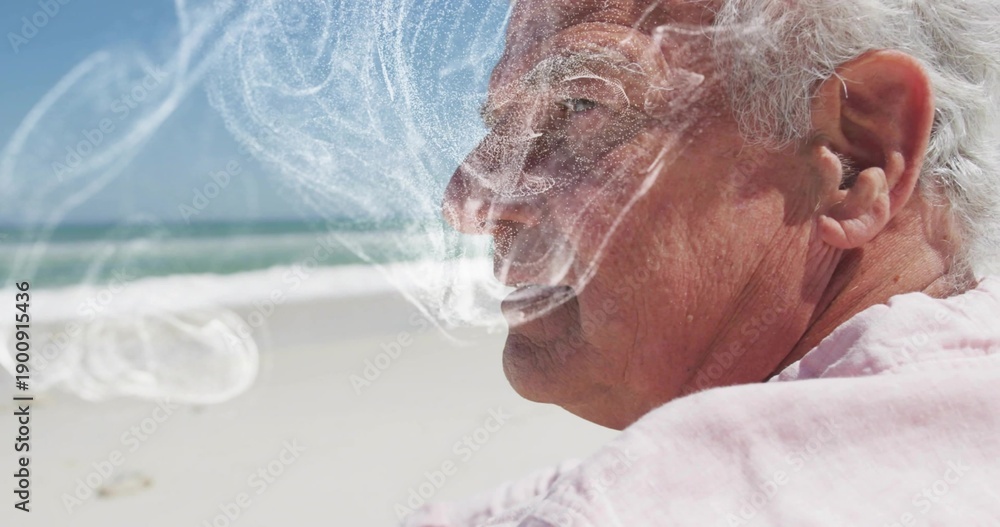 Fototapeta premium Exhaling senior man wearing pale pink collared shirt at beach shoreline, vapor swirling