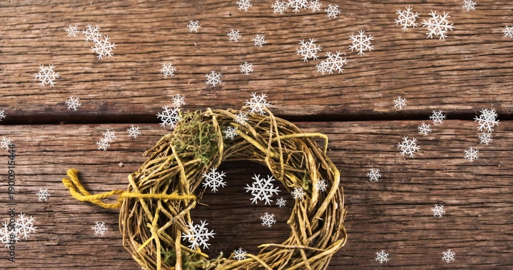 Fototapeta premium Displaying grapevine wreath with moss and yellow twine on weathered planks, scattering snowflakes