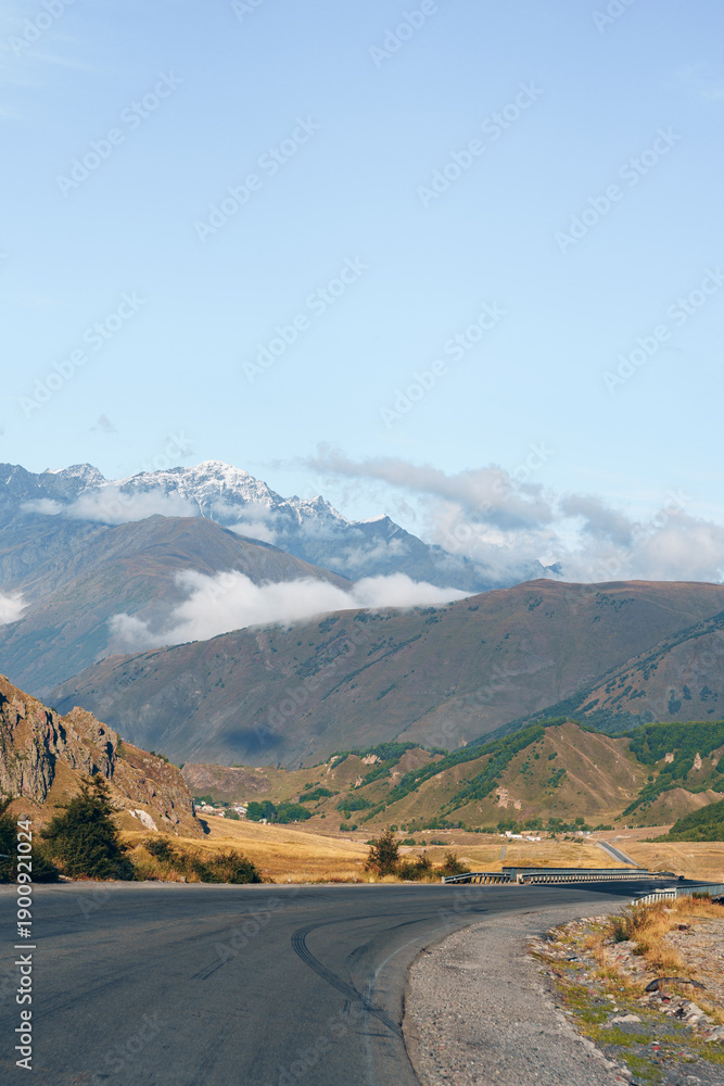 Fototapeta premium Scenic road leads through mountains and valleys under blue sky during daylight