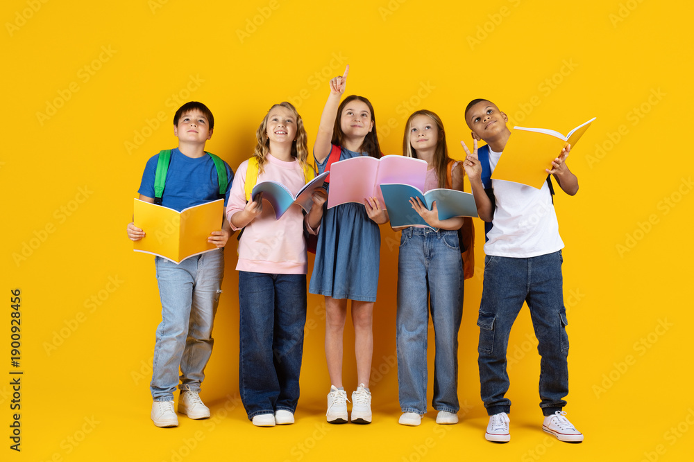 Obraz premium Preteen children looking up with books in hands on yellow studio background. Curious expressions symbolize learning, imagination, school education, and future goals