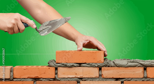 A hand places a brick on a wall with cement and a trowel