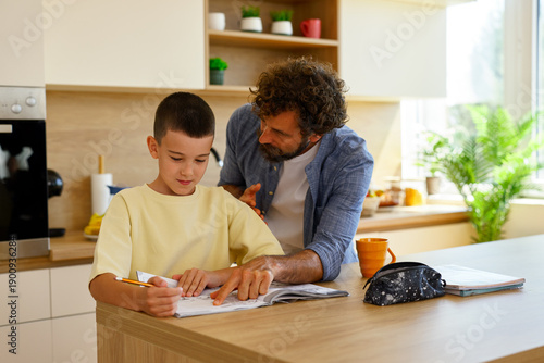 Father helping son with homework in modern kitchen