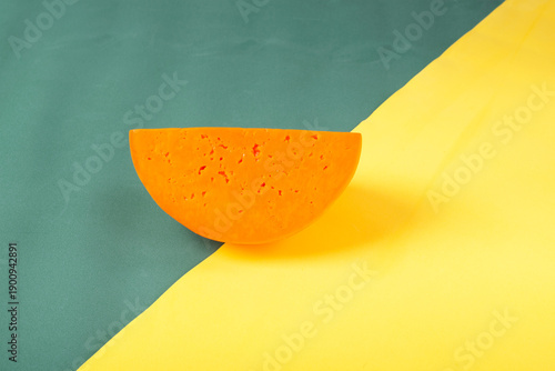 Piece of orange cheese colored with carrot juice on yellow and green background