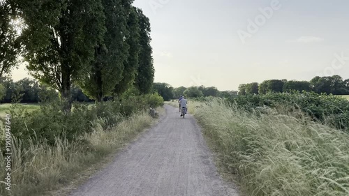 4K UHD video footage of a straight countryside gravel road bordered by grass and trees, with an unrecognizable person in the distance.
