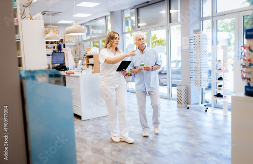 Female pharmacist helps a senior man choose medication in pharmacy.