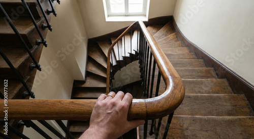 Person holding wooden handrail looking down spiral staircase.