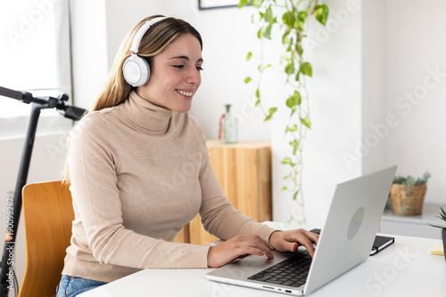Young adult businesswoman working happily on laptop. Professional woman focusing on her tasks with a smile. Productivity and motivation concept.