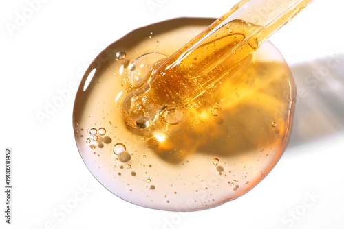 glass pipette dropper close up and Liquid yellow-orange retinol or vitamin c gel or serum on a petri dish on blue background. Cosmetics lab research