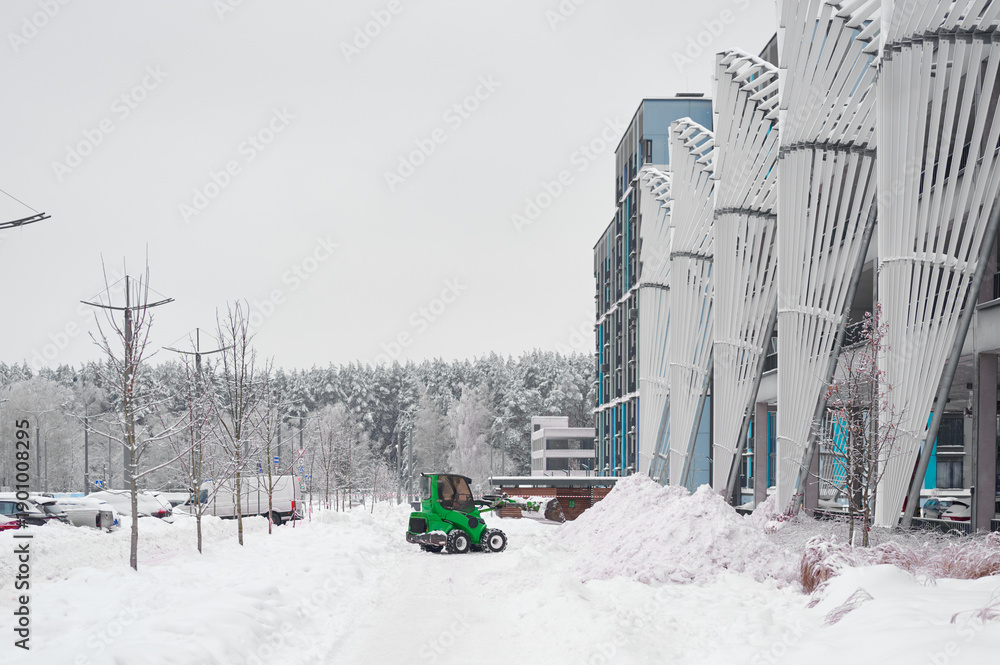 Naklejka premium Tractor clearing snow near building in winter