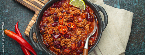 Mexican dish Chili con carne with lime, garlic and chili pepper on dark background top view