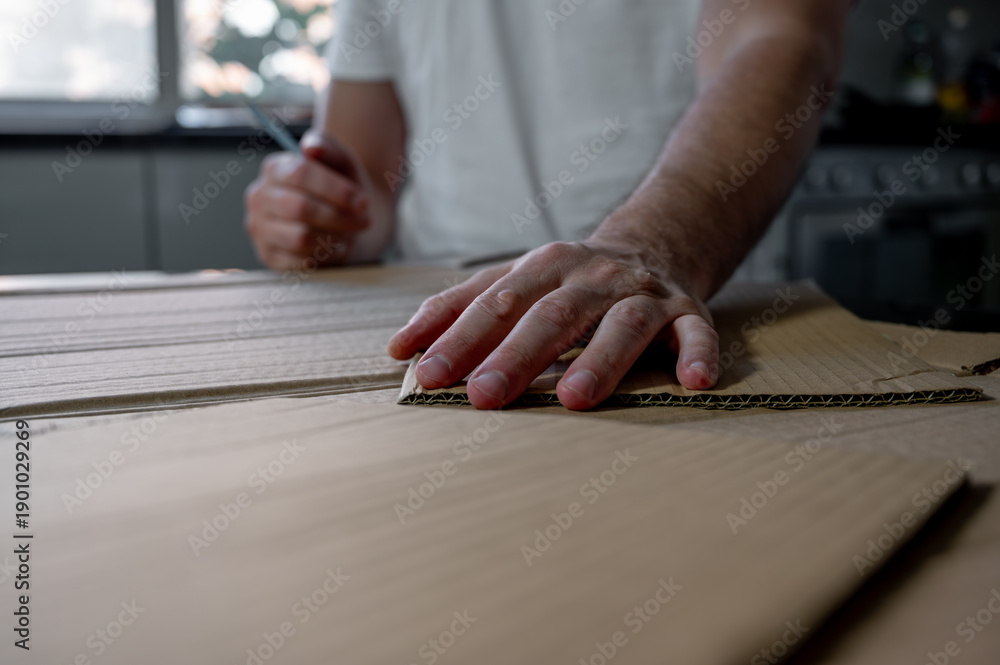 Obraz premium Close-up of hands crafting a cardboard sword on a table using cardboard, colored paper, and glue. DIY handmade project, creativity and imagination concept, eco-friendly hobby and recycled materials.