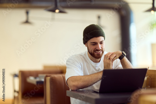 Bild auf Leinwand Casual Diner Work Session: Man in Beanie Using Laptop and Relaxed Smile