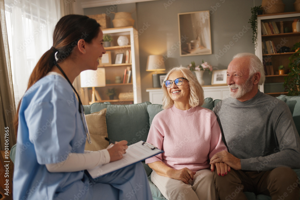 Fototapeta premium Home health nurse interacts with an elderly couple during a routine health check-up at their house. The couple looks engaged and comfortable in their living room while the nurse takes notes.