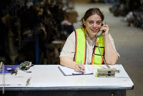 Worker on the phone at a desk, taking notes in a warehouse setting