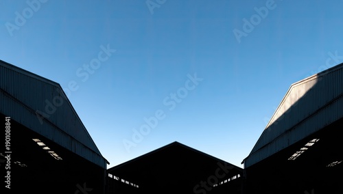 Symmetrical industrial rooftops against a bright blue sky