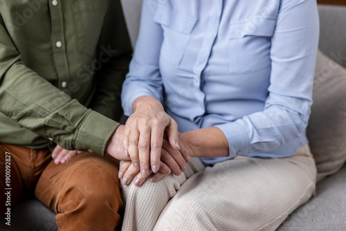 Mature man gently placing his hand over an older woman's hand, conveying care, empathy, and a strong connection between them while seated together on a sofa