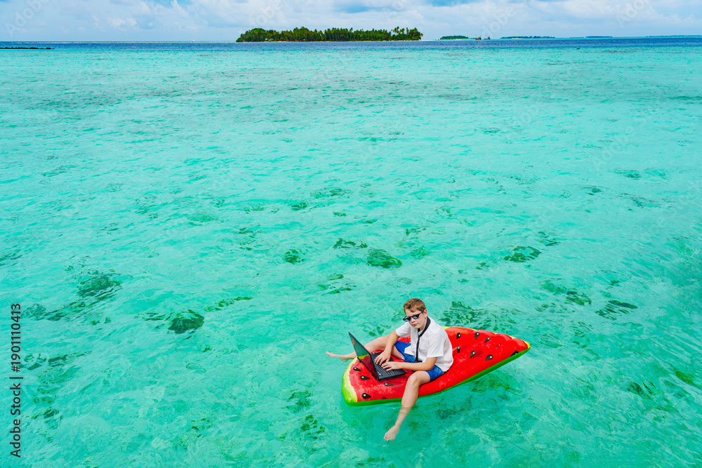 Fototapeta premium Young business boy. child in glasses works on a tropical island.