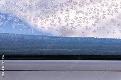 Snowflakes and frost patterns on a cold window with snow outside. Cozy winter atmosphere from indoors, seasonal background with copy space, soft natural light and minimal composition.