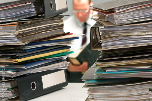 Tableau sur toile Gestresster Büromitarbeiter mit Aktenordner beim telefonieren zwischen zwei Aktenstapeln