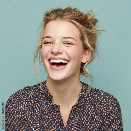 A young woman laughs joyfully while wearing a navy shirt. She has light hair and is against a blue background
