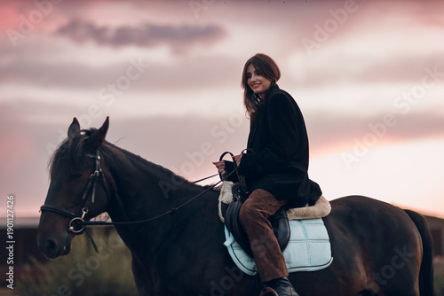 Young woman in black with her horse at sunset outdoors