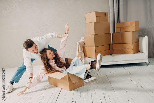 Happy young family couple man haul woman inside box. Moving with cardboard boxes to new estate home apartment concept