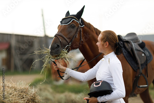 Woman rider jockey feeds horse at stable