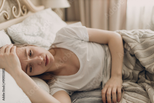 Young woman suffering with headache flu ill sick disease cold at home indoor lying on bed top view