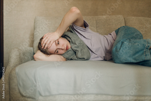 Young woman wearing scarf has flu ill sick disease cold at home indoor lying on sofa