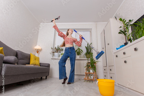 Woman dances while cleaning her home in a bright apartment during the day with plants around her