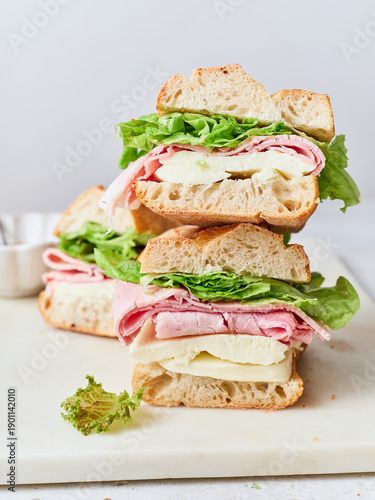 Healthy sandwich with mozzarella cheese, lettuce, ham, and baguette on a lunch table with fresh ingredients
