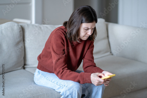 Foto Stressed woman frowning while checking smartphone, scrolling social media sits on sofa at home
