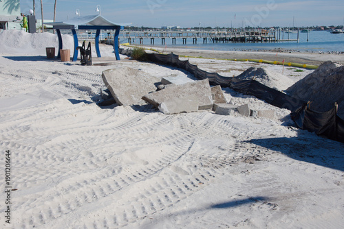 Beach Restoration Construction Site With Yellow Barricade Tape, Seagulls, and Waterfront Pavilion on a Sunny Day in Gulfport, FL. Marked by bright yellow tape, sandy foreground, seagulls in flight, an