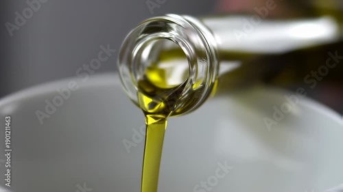 Olive oil pouring from a glass bottle into a white bowl