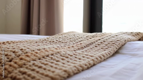 A beige, textured crocheted or knitted blanket rests on a white bed
