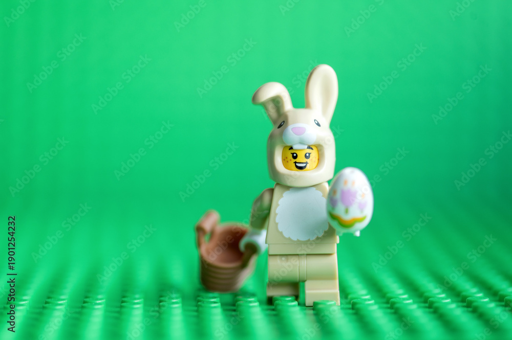 Fototapeta premium Lego minifigure Easter bunny with eggand basket on a green background. Happy Easter concept.