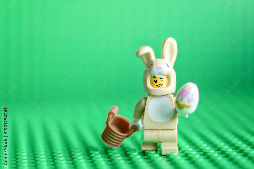 Naklejka premium Lego minifigure Easter bunny with egg on green background. Easter holiday concept.