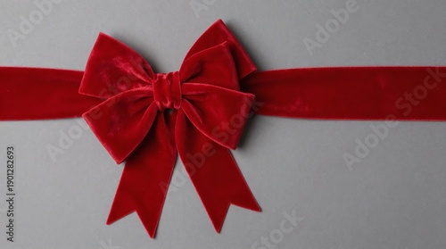 A red velvet bow tied on a ribbon against a gray background