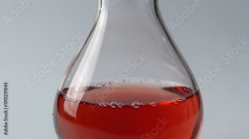 A close-up view of a glass flask filled with a vibrant red liquid on a plain background