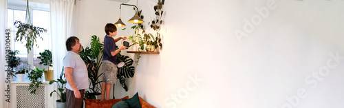 Father and teenage son caring for indoor plants at home, family bonding and sustainable lifestyle, banner