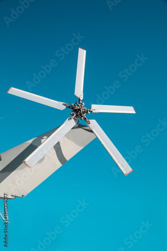 The helicopter's tail rotor is silver against the blue sky on a clear sunny day.   Helicopters Military equipment atom airplanes.
