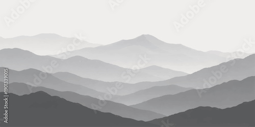 A misty mountain landscape at sunrise reveals a vast range of peaks and forest hills shrouded in blue fog and clouds above a deep valley