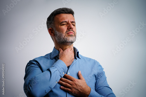 Businessman having sore throat and touching his neck, wearing a blue shirt against light grey background. Hard to swallow