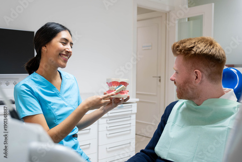 Dental professional demonstrating oral hygiene using a jaw model to a patient in a clinic