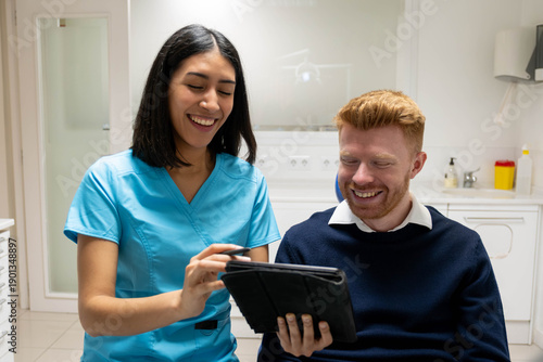Dental assistant discussing treatment using a digital tablet with a smiling patient