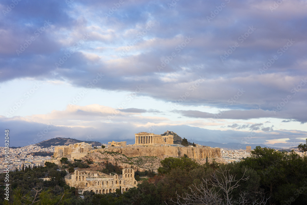 Fototapeta premium The Acropolis and Parthenon in Athens, at sunset, Greece. Bathed in the light of the setting sun against a backdrop of picturesque clouds, the Acropolis looks majestic and grandiose.