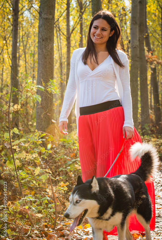 Fototapeta premium The girl is walking along the forest with her husky dog