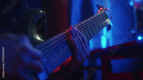 A person plays an electric guitar on stage in a small venue. Colorful lights shine around creating a lively atmosphere