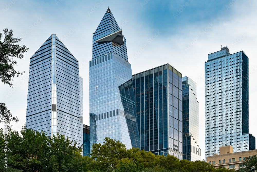 Obraz premium The modern glass skyscrapers of Hudson Yards rise above the green treetops of Manhattan in New York City.